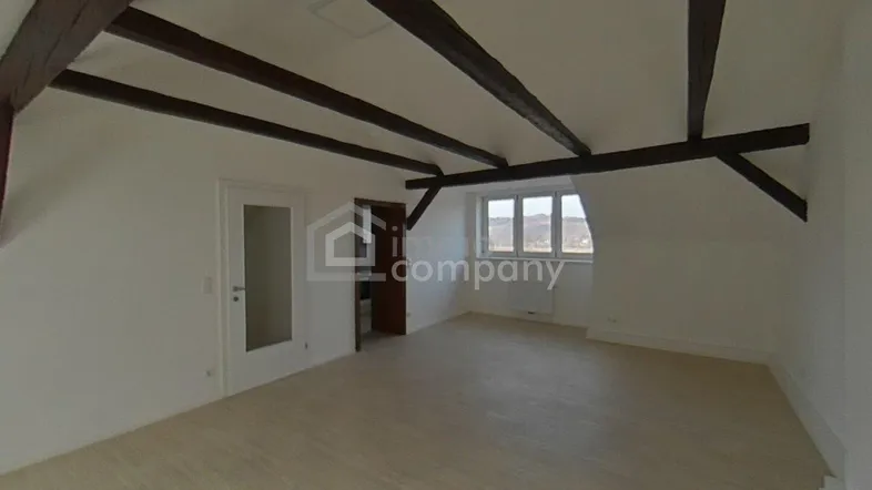 Helles Dachzimmer mit sichtbaren Holzbalken und schrägen Wänden, bietet viel Potenzial zur individuellen Gestaltung.