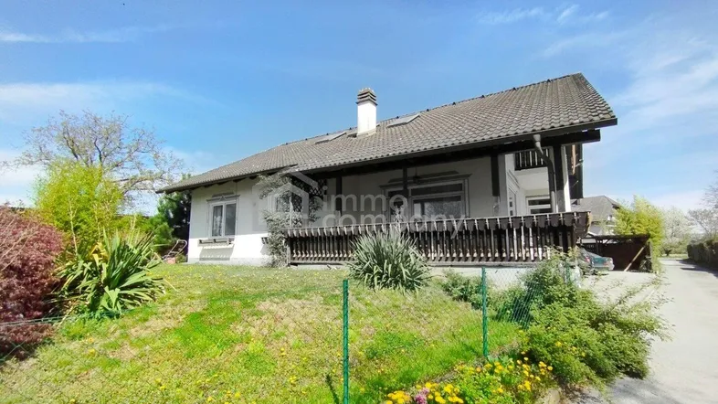 Freistehendes Haus mit großem Garten und einer Holzterrasse unter blauem Himmel.