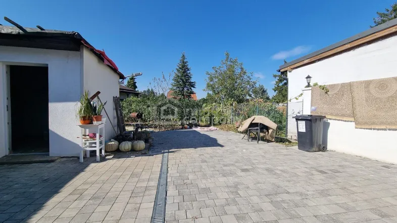 Gepflasterter Innenhof zwischen Gebäuden mit Pflanzen und Kürbissen unter blauem Himmel.