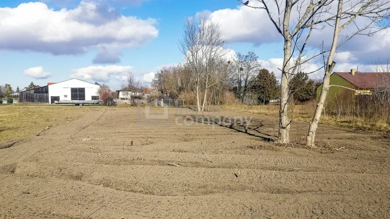 Weitläufiges Grundstück mit vorbereitetem Boden und Blick auf die ländliche Umgebung unter blauem Himmel.