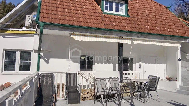 Geräumige Außenterrasse mit Sitzgelegenheiten, Markise und Blick auf das Haus mit Ziegeldach.