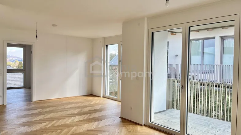 Helles, leeres Zimmer mit Fischgrätparkettboden und Zugang zu einem Balkon.