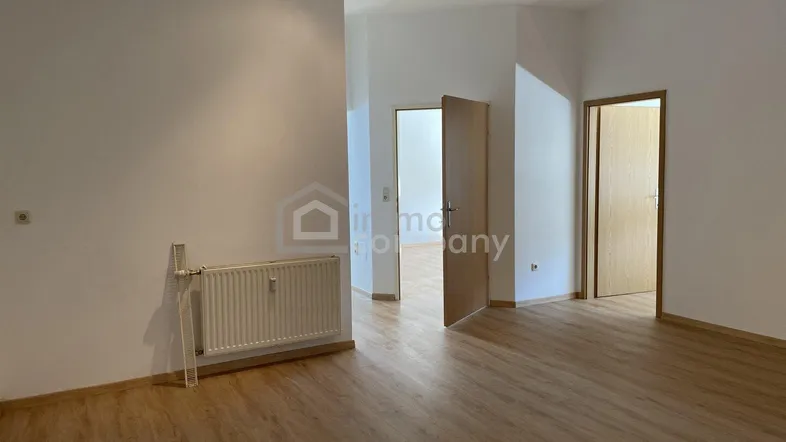 Helles, leeres Zimmer mit Laminatboden und Heizkörper, das als Wohnbereich genutzt werden könnte.