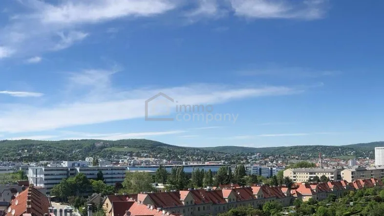 Panoramablick über eine Stadt mit grünen Hügeln im Hintergrund und verschiedenen Wohngebäuden.