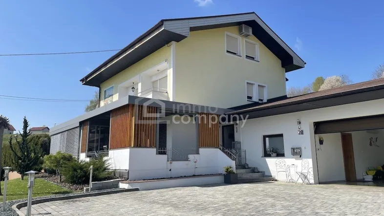 Vorderansicht des Hauses mit gepflasterter Auffahrt, Garage und modernem Eingangsbereich unter blauem Himmel.
