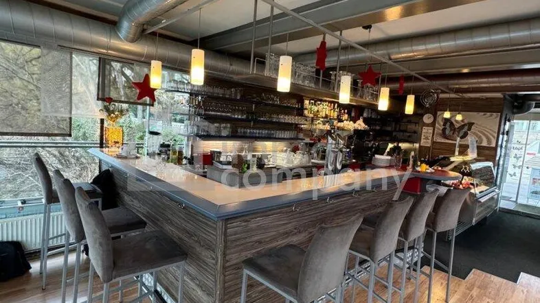 Moderne Bar mit Holzboden, hohen Decken und industriellen Lüftungsrohren, ideal für Gastronomie.