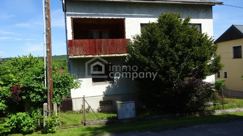Vorderansicht eines älteren Hauses mit kleinem, verwittertem Holzbalkon und Vorgarten.