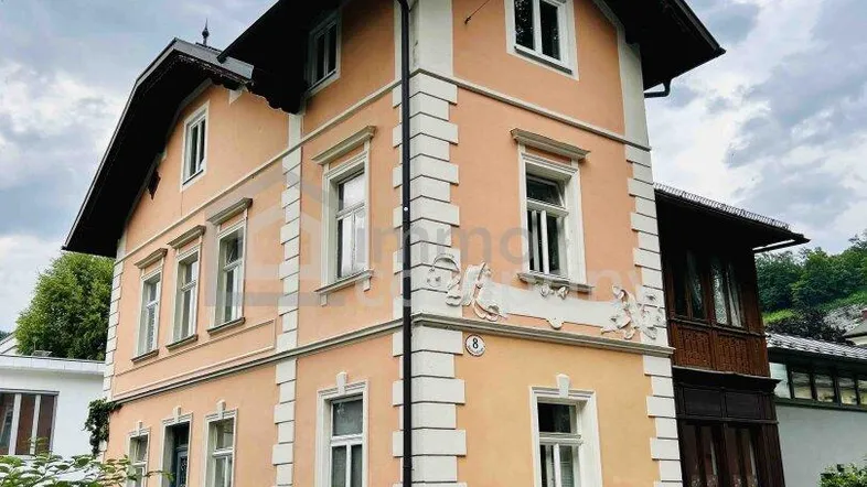 Klassisches Mehrfamilienhaus mit traditioneller Architektur und dekorativen Fassadenelementen unter bewölktem Himmel.