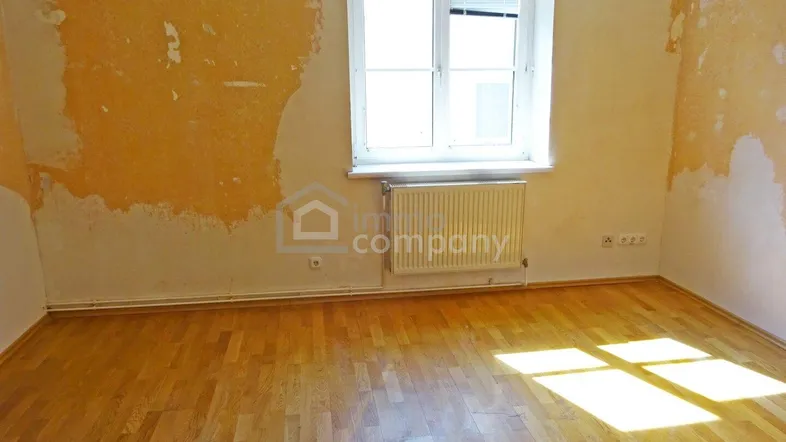 Leeres Zimmer mit abblätternder Tapete und Holzfußboden, bereit für eine Renovierung.
