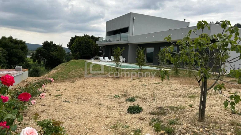Moderne Villa mit Pool und weitläufigem Grundstück unter bewölktem Himmel.