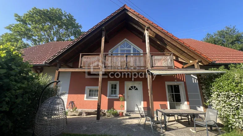 Rotes Landhaus mit Balkon, Terrasse und Gartenbereich unter blauem Himmel.