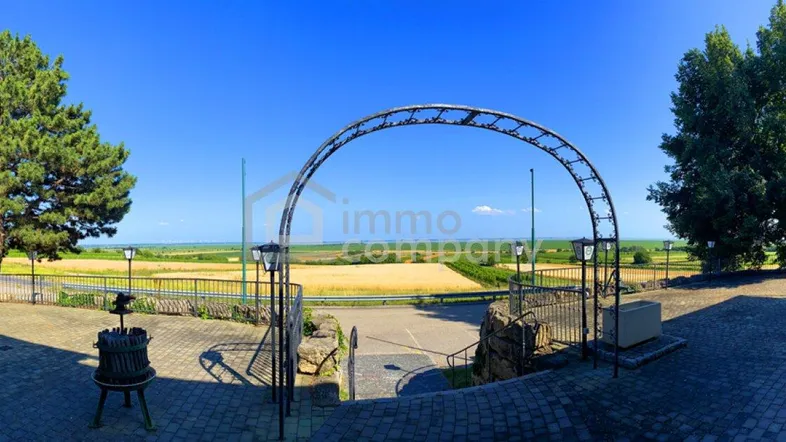 Weitläufiger Außenbereich mit gepflastertem Weg, einem dekorativen Bogen und Blick auf die Landschaft.
