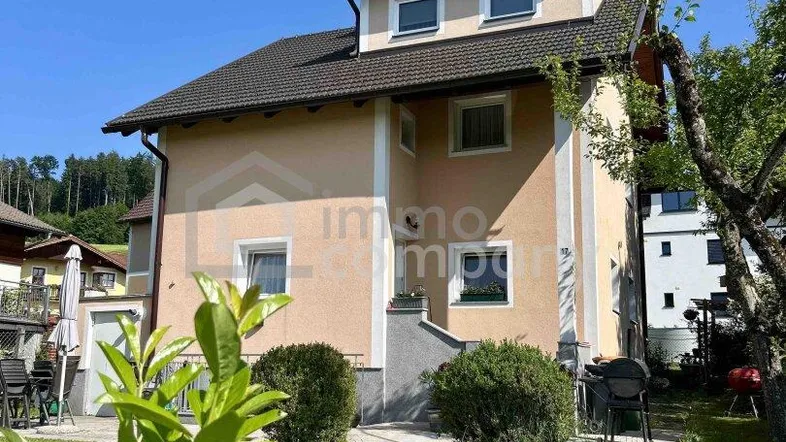Freistehendes Haus mit gepflegtem Garten und sonniger Fassade unter blauem Himmel.