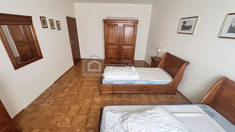 Schlafzimmer mit zwei Betten, Holzschrank und Parkettboden in Fischgrätmuster.