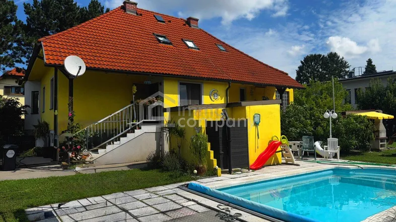 Gelbes Haus mit rotem Ziegeldach, großem Garten, Swimmingpool und Spielbereich im Freien.