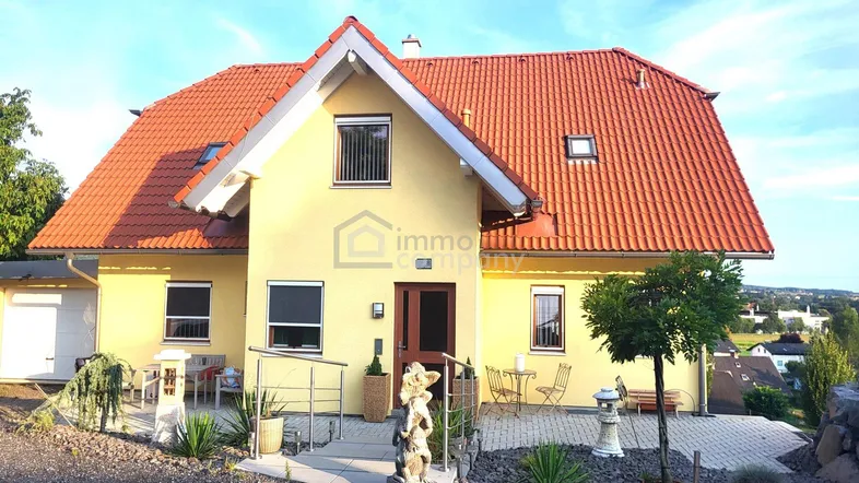 Gepflegtes Einfamilienhaus mit gelber Fassade, rotem Satteldach und schöner Gartenanlage.