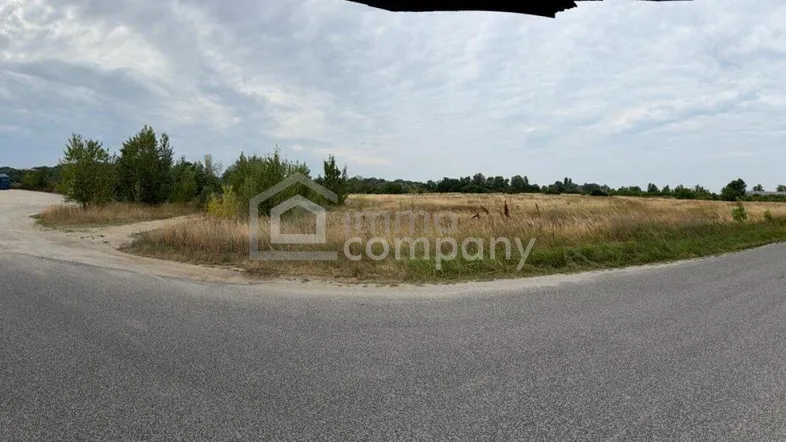 Weitläufiges unbebautes Grundstück neben einer Straße unter bewölktem Himmel, ideal für zukünftige Entwicklung.