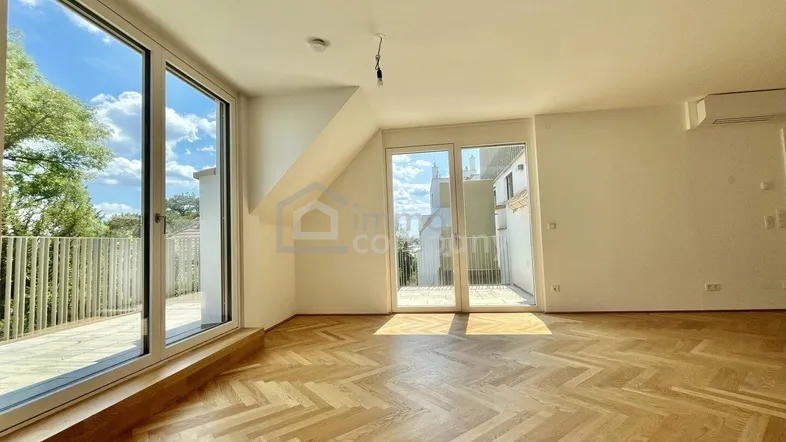 Helles Zimmer mit Fischgrätparkett und Zugang zu einem Balkon, bietet viel natürliches Licht.