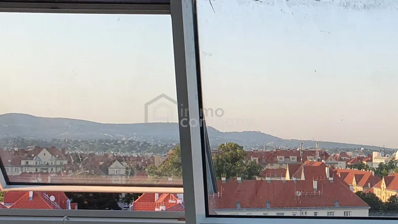 Blick aus einem Fenster auf eine Stadtlandschaft mit roten Dächern und dahinterliegenden Bergen.