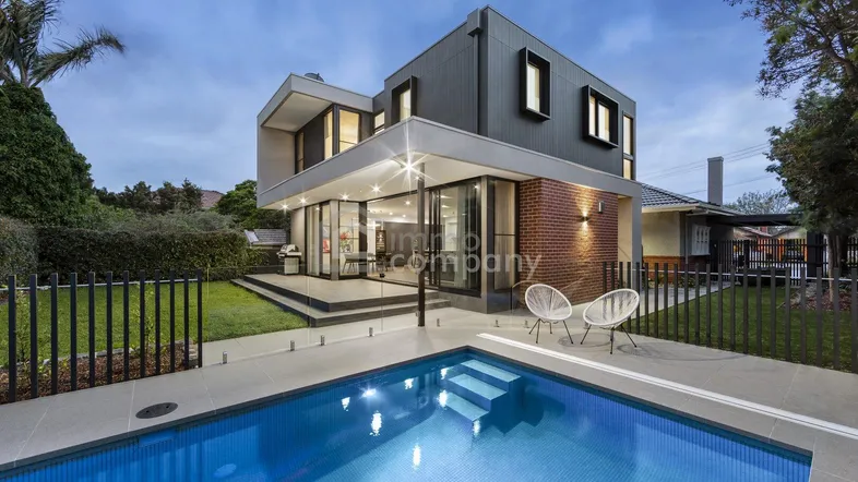 Modernes Haus mit Pool und Terrasse, umgeben von einem gepflegten Garten unter abendlichem Himmel.