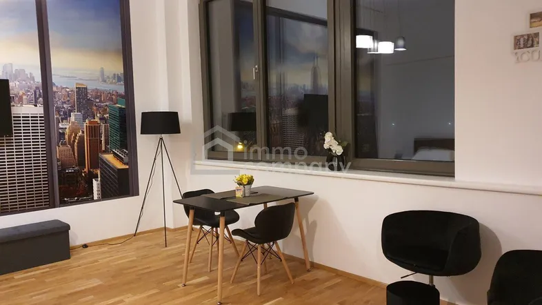 Heller Wohnbereich mit Holzboden, Esstisch und großen Fenstern, die viel Tageslicht hereinlassen.