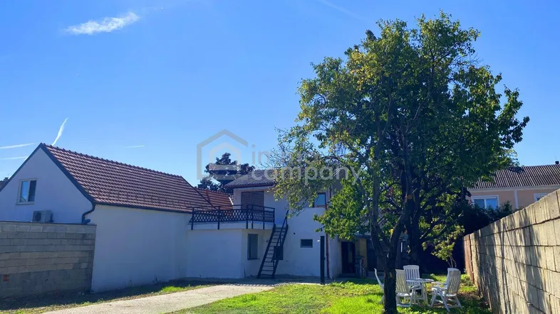 Blick auf das Haus von hinten mit Rasenfläche und einfacher Sitzgelegenheit im Freien.