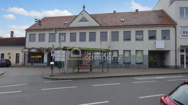 Ansicht des Geschäftsgebäudes von der Straße mit Bushaltestelle und umliegenden Geschäften.