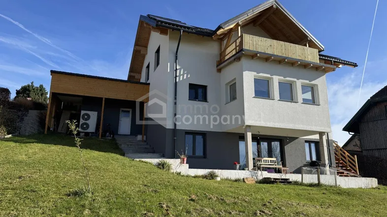 Modernes Einfamilienhaus mit Satteldach, Photovoltaikanlage und Gartenbereich auf einem Hanggrundstück.