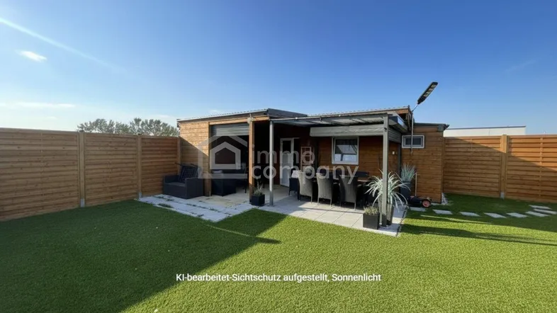 Sonniger Gartenbereich mit Kunstrasen, Terrasse und gemütlicher Sitzecke, umgeben von einem Holzzaun.