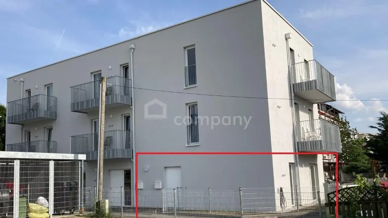 Modernes Mehrfamilienhaus mit Balkonen und einem kleinen eingezäunten Bereich im Vordergrund.