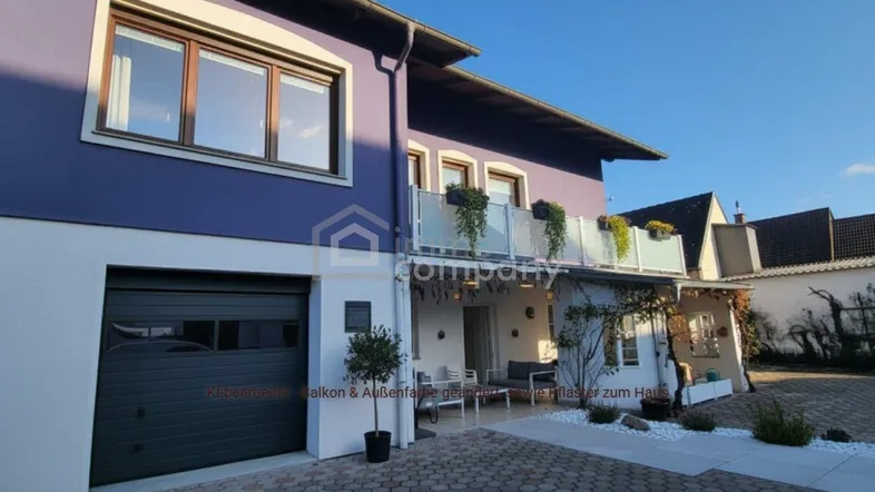 Modernes Haus mit lila Fassade, integrierter Garage und kleinem Balkonbereich.