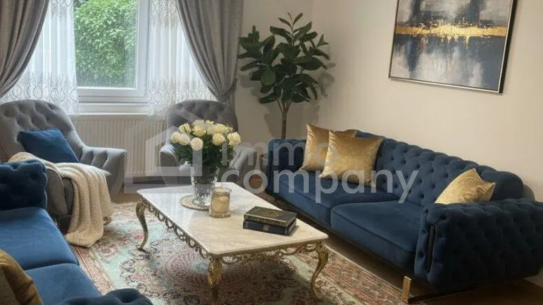 Elegantes Wohnzimmer mit blauen Samtsofas, Holzboden, Kronleuchter und Blick ins Grüne.