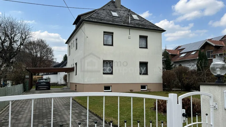 Einfamilienhaus mit weißer Fassade, Satteldach und Carport im Vorgarten.