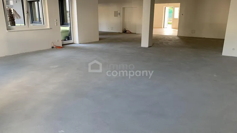 Großer, leerer Innenraum mit Betonboden, weißen Wänden und Säulen, bereit für den Ausbau.