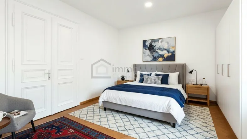 Helles Schlafzimmer mit Parkettboden, großem Bett und weißen Einbauschränken, modern eingerichtet.
