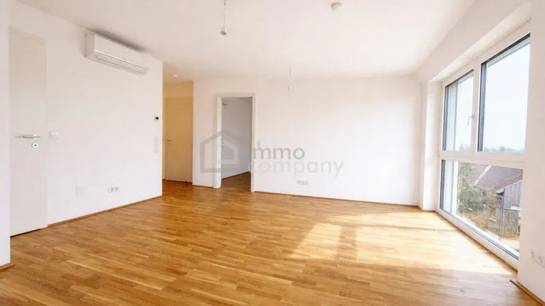 Geräumiges, leeres Zimmer mit hellem Parkettboden, großen Fenstern und Klimaanlage.