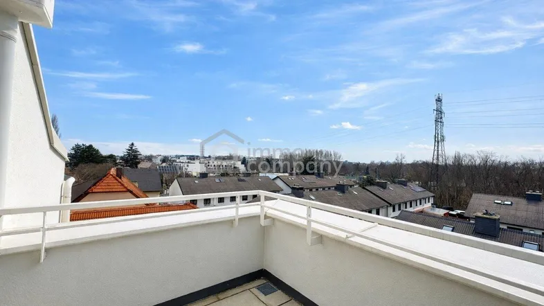 Blick über die Dächer der Stadt von einem Balkon unter blauem Himmel.