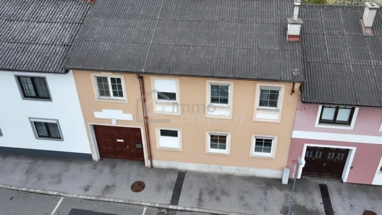 Luftaufnahme von Reihenhäusern mit grauen Dächern und einer Straße davor.