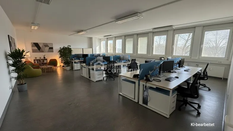 Geräumiges Großraumbüro mit mehreren Arbeitsplätzen, einem Loungebereich und großen Fenstern für viel Tageslicht.