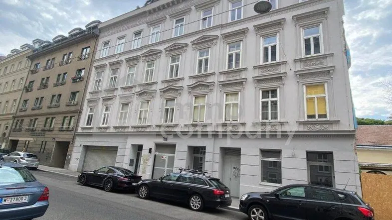 Historisches Mehrfamilienhaus mit klassischer Fassade und parkenden Autos an der Straße.