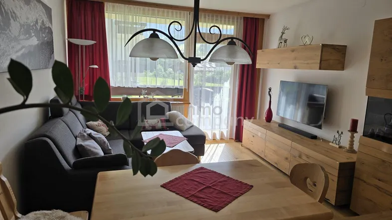 Heller Wohnbereich mit Holzboden, gemütlichem Sofa und Zugang zum Balkon mit Bergblick.