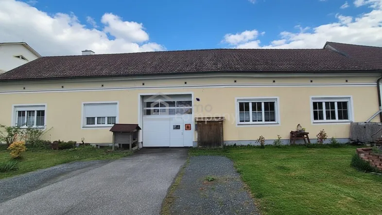 Einfamilienhaus mit heller Fassade, braunem Ziegeldach, mehreren Fenstern mit Rollläden und großer Garagentür.