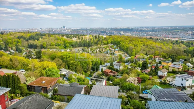 Panoramablick über eine grüne Wohngegend mit Häusern, Bäumen und der Skyline einer Stadt in der Ferne.