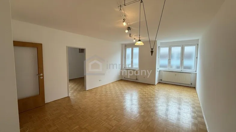 Helles Zimmer mit Fischgrätparkettboden und großen Fenstern, bereit zur individuellen Gestaltung.