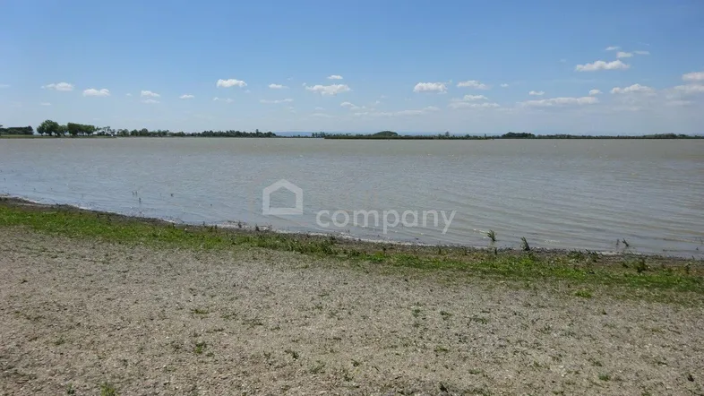 Weitläufiger Blick über einen See unter blauem Himmel mit leichter Bewölkung und Uferbereich.