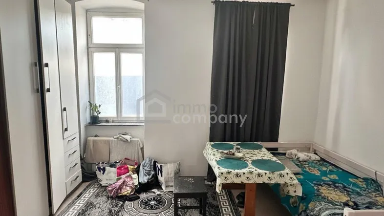 Schlafzimmer mit Einzelbett, Kleiderschrank und Teppichboden in einem Altbau.