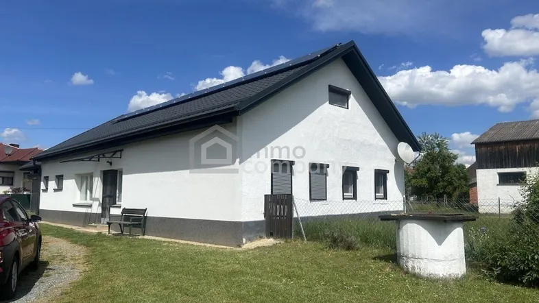 Weißes Einfamilienhaus mit schwarzem Satteldach und Solarpaneelen auf dem Land.