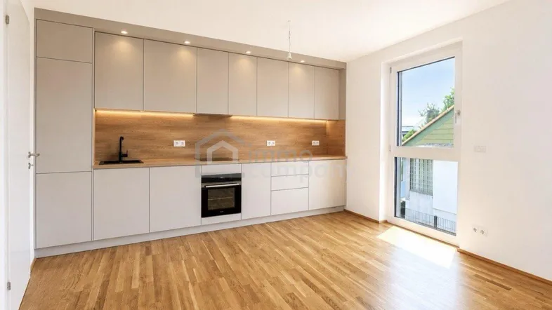 Moderne Einbauküche in hellem Grau mit Holzakzenten und Parkettboden in einem offenen Wohnbereich.
