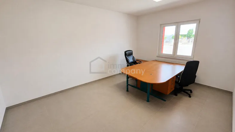 Geräumiges Büro mit einem großen Schreibtisch, zwei Stühlen und einem Fenster, das viel Tageslicht hereinlässt.