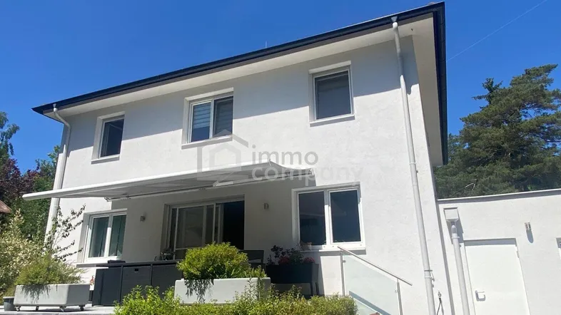 Modernes Einfamilienhaus mit heller Fassade, großen Fenstern und einer gepflegten Terrasse mit Gartenbereich.